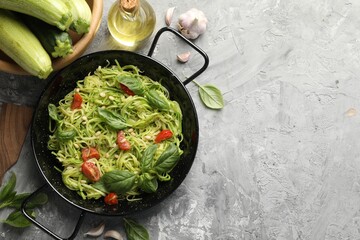 Tasty zucchini noodles with tomatoes, pine nuts, basil and ingredients on grey table, flat lay. Space for text