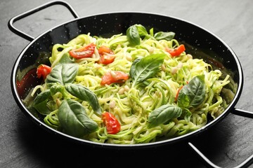 Tasty zucchini noodles with tomatoes, pine nuts and basil on black table, closeup