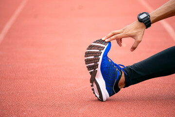 Close-up of athlete stretching leg on running track while holding bright blue sneaker with copy...