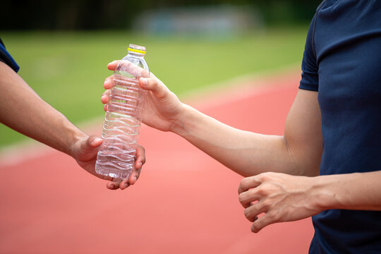 Close-up of two athletes hands exchanging a plastic water bottle on outdoor running track during workout