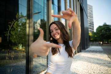 Young woman framing the future with her hands, smiling at new possibilities in urban setting