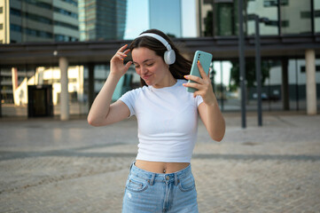 Young woman dancing and listening to music with headphones and smartphone in a city setting