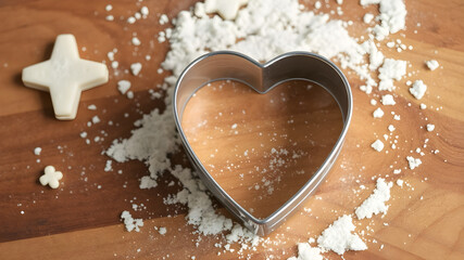 A heart-shaped cookie cutter on a wooden cutting board with scattered flour