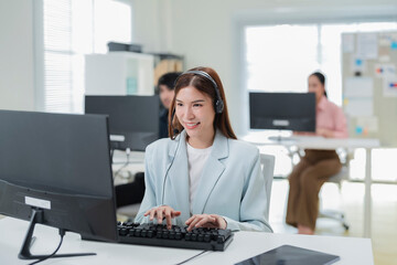 Happy businesswoman with headphones working on PC in call center office, young female technical...