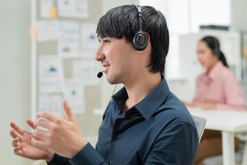 Happy businessman with headphones working on PC in call center office, young male technical support...