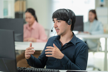 Happy businessman with headphones working on PC in call center office, young male technical support...