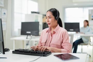 Happy businesswoman with headphones working on PC in call center office, young female technical...