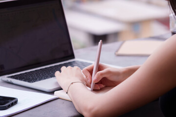 Asian adult hands working planning writing notes using laptop notebook pen smartphone outdoors cafe modern digital professional productivity focus study remote education entrepreneur