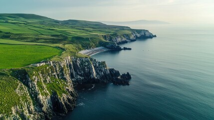 A breathtaking aerial view of a rugged coastline with lush green fields and rocky cliffs extending into the ocean, with a distant mountain range