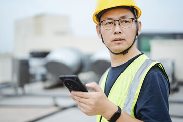 asian engineer working on smart phone with  external unit of commercial air conditioning and...