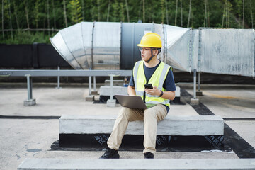 asian engineer working on laptop with  external unit of commercial air conditioning and ventilation...