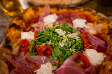 A vibrant Italian pizza features a crispy crust topped with fresh tomatoes, arugula, creamy cheese, and savory cured meats, enjoyed in a warm, inviting restaurant atmosphere during dinner time.