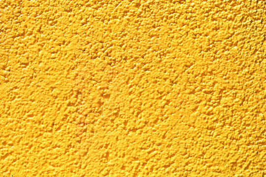 Yellow rough plastered wall surface. Grunge stucco texture in vivid color. Bright grainy facade close-up. Decorative cement rendering background. Abstract building detail for construction themes.