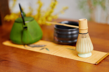 Serene tea ceremony arrangement with green cast iron teapot, bamboo whisk, and bamboo vessel on wooden table, emphasizing tranquility and cultural tradition in a modern aesthetic