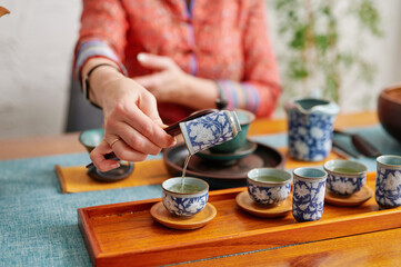 Woman pouring tea from ornate teapot into patterned cups, surrounded by detailed teaware on a wooden table, capturing cultural heritage and mindful ritual in an elegant, peaceful atmosphere