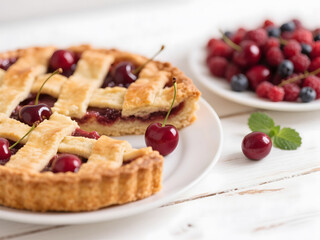Whole cherry pie with lattice crust served with fresh berries on white rustic table in soft natural daylight, one slice missing