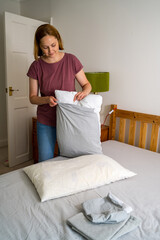 Woman changing pillow case with fresh clean grey cotton bed sheets