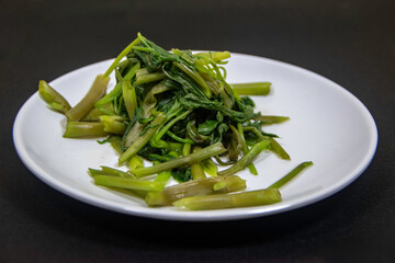Photograph, boiled kangkung (water spinach) presented on a clean, white plate – isolated on white background.