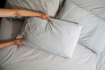 Female hands holding a pillow with fresh clean pillowcases, grey cotton bed sheets