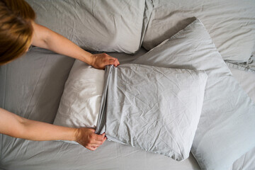 Female hands holding a pillow with fresh clean pillowcases, grey cotton bed sheets