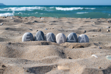 Stone with the word Ellada on sandy beach background