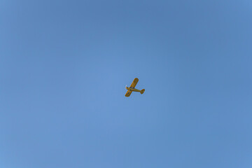 Small yellow airplane flying in clear blue sky during daytime in a serene setting