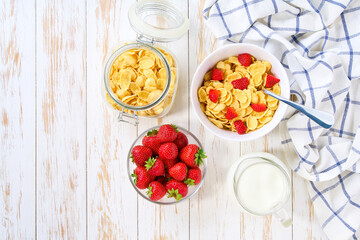 Healthy breakfast with corn flakes and strawberry on a white wooden table, top view.
