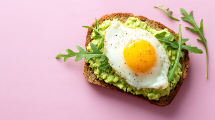 Deliciously healthy avocado toast topped with a perfectly fried egg and fresh greens on a pink background