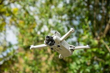 Mini drone captured in mid-flight with a backdrop of green trees, showcasing modern aerial technology in a natural outdoor environment.