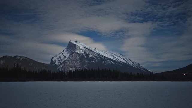 Night time lapse of Mount Rundle and a frozen lake with moving clouds