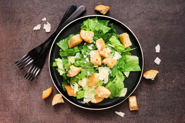 Classic Caesar salad with croutons and parmesan cheese. Above view table scene on a dark background.