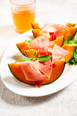Cantaloupe melon with prosciutto and fresh basil, on a white plate, natural light,