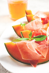Cantaloupe melon with prosciutto and fresh basil, on a white plate, natural light,