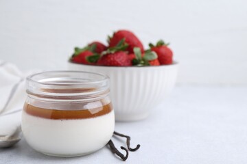Tasty panna cotta with caramel, vanilla pods and strawberries on light table, closeup. Space for text