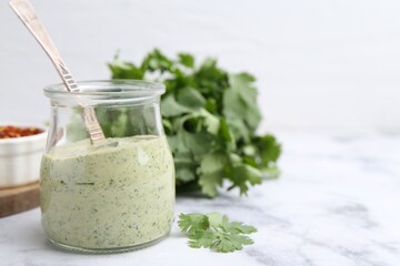 Tasty cilantro sauce and spoon in jar on light marble table, closeup. Space for text