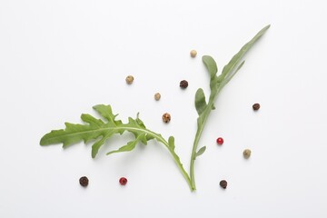 Fresh ripe green arugula leaves and peppercorns on white background, flat lay