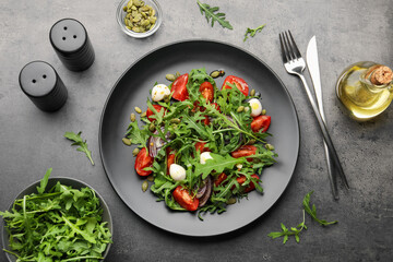 Tasty salad with arugula, mozzarella and vegetables served on grey table, flat lay