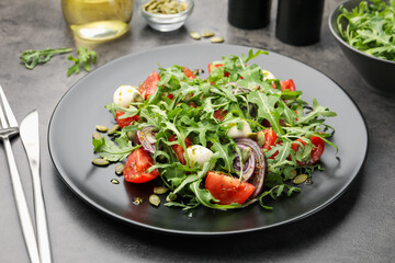 Tasty salad with arugula, mozzarella and vegetables served on grey table, closeup