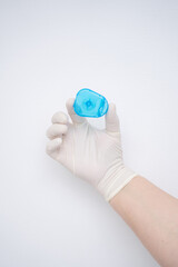 A hand is firmly holding a blue colored medical sample container inside a gloved hand
