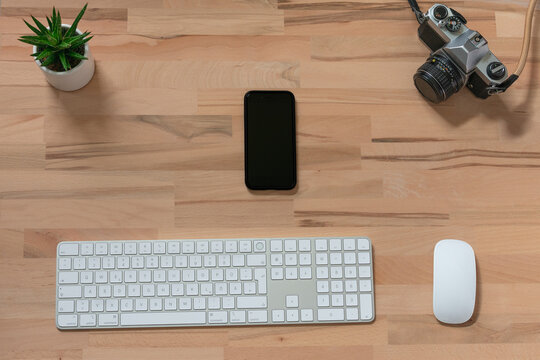 workspace of modern wireless white keyboard and mouse, smartphone and analog film camera on wooden table with a green plant in flowerpot. top view with copy space.