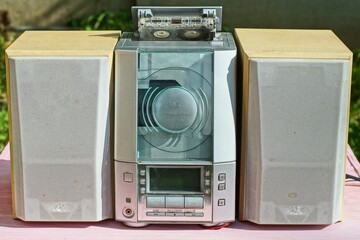 Obraz premium one small gray plastic electric old with buttons musical cassette player with powerful wooden stereo music acoustic speakers stand on pink wooden table day outside