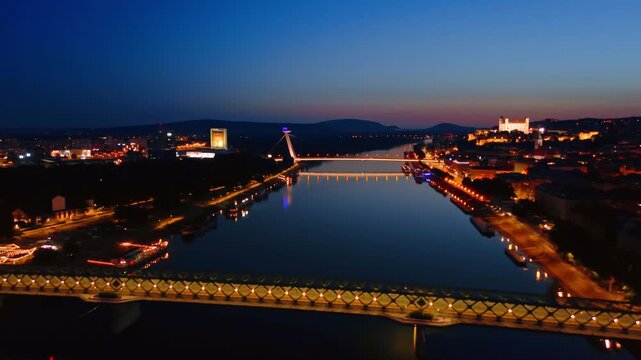 Footage above the peaceful waterscape of the Danube at night. Lights are on at the bridges above the river. Bratislava, Slovakia.