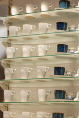 Row of white ceramic espresso mugs and blue cups on glass shelves