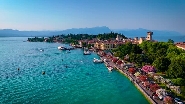 Aerial photo of scenic Sirmione on Lake Garda, Italy, featuring Scaliger Castle, waterfront promenade, boats, and lush gardens. Ideal for travel, tourism, and real estate marketing