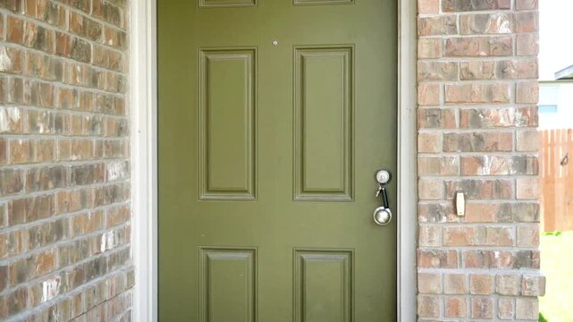 An olive green front door is framed by brick on a house