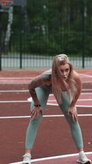 Young blonde woman in sportswear doing stretching exercises standing on basketball court in the...