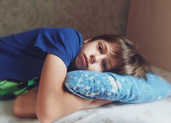 Sad teenager boy in melancholy alone on bed in his bedroom. child has a thoughtful look.