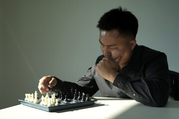 Vertical selective focus shot of stressed man is making chess move in dark room. Smart intelligent man playing logical board game alone at home, planning and strategic moves in the business sector.