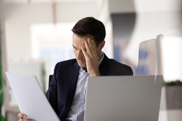 Businessman read document with shocked, distressed expression at workplace, facing serious issues,...