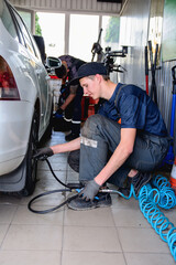Tire service technicians inflate car tires with air and tighten them with a torque wrench inside the service center in their work uniforms